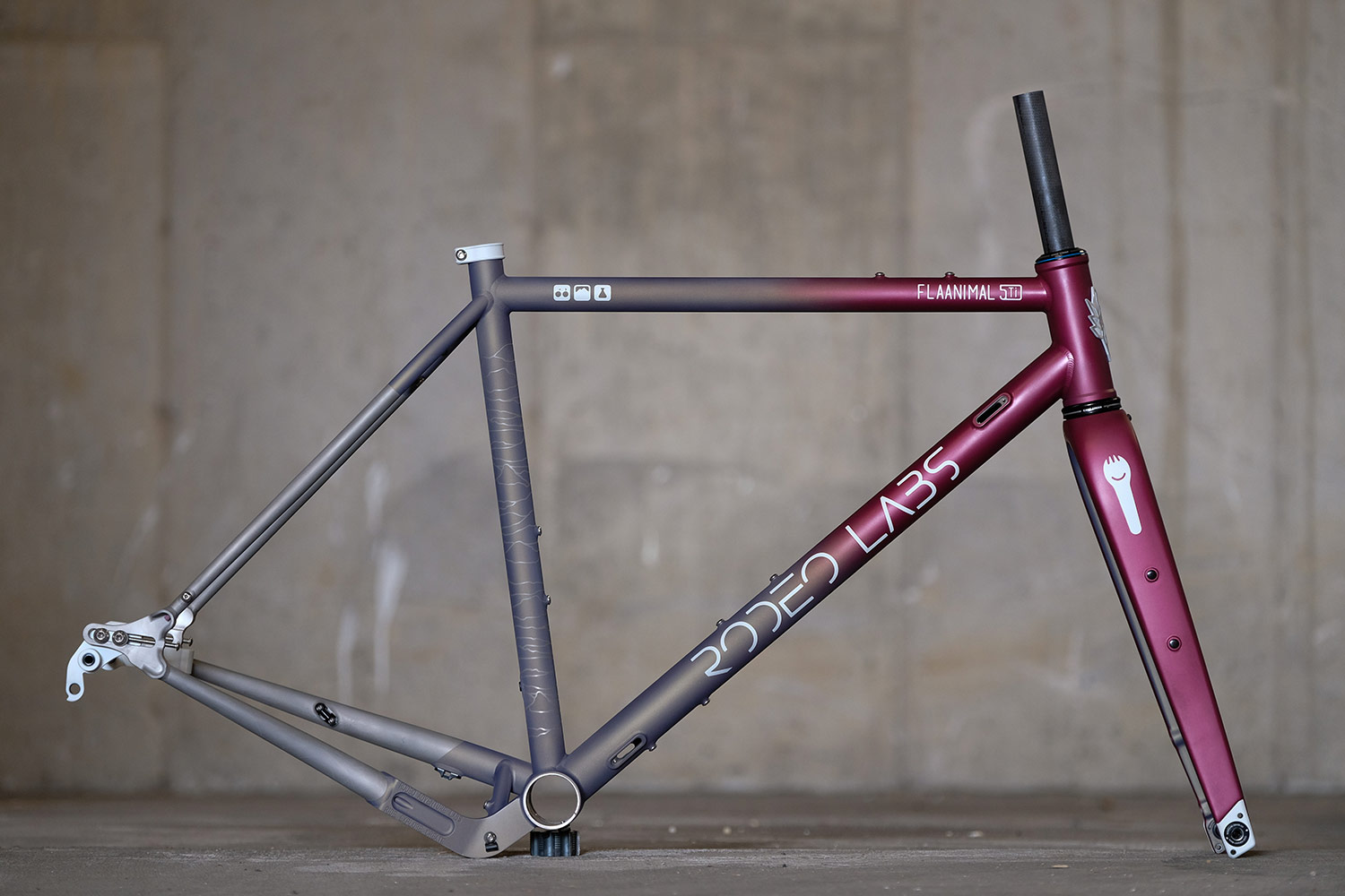 Magenta, grey, and brown fade custom cerakote Rodeo Labs Flaanimal steel gravel bike frame with topo lines on bicycle seat tube.