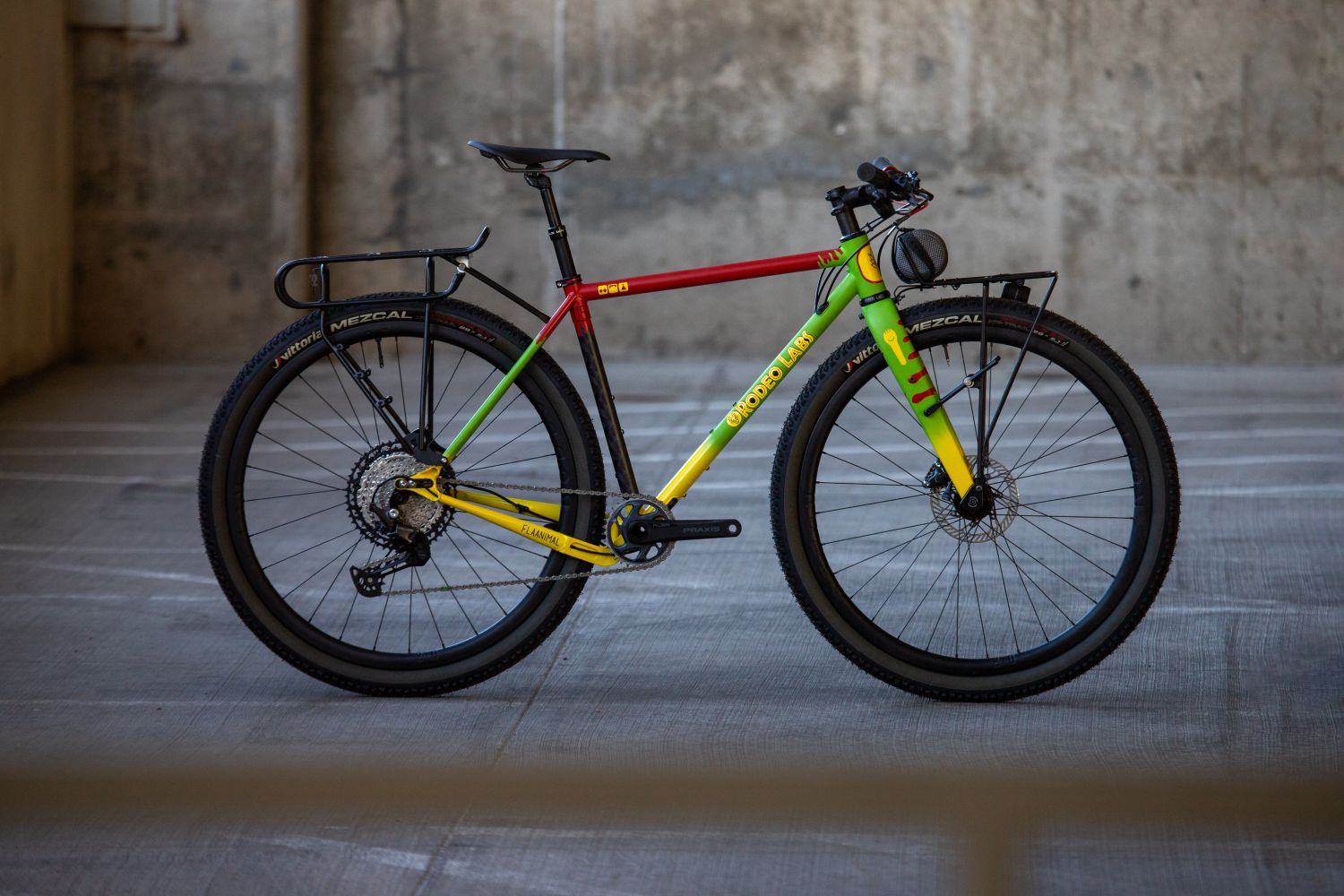 Rodeo Labs Flaanimal 5 steel gravel bike with a custom cerakote paint job made to look like the Jurassic Park Ford Explorer. The bicycle is red, green, and yellow like the Jurassic Park Explorers were for the park's tour vehicles, not the red and white Jeeps the Jurassic Park employees used. The bike has front and rear racks and flat bars.